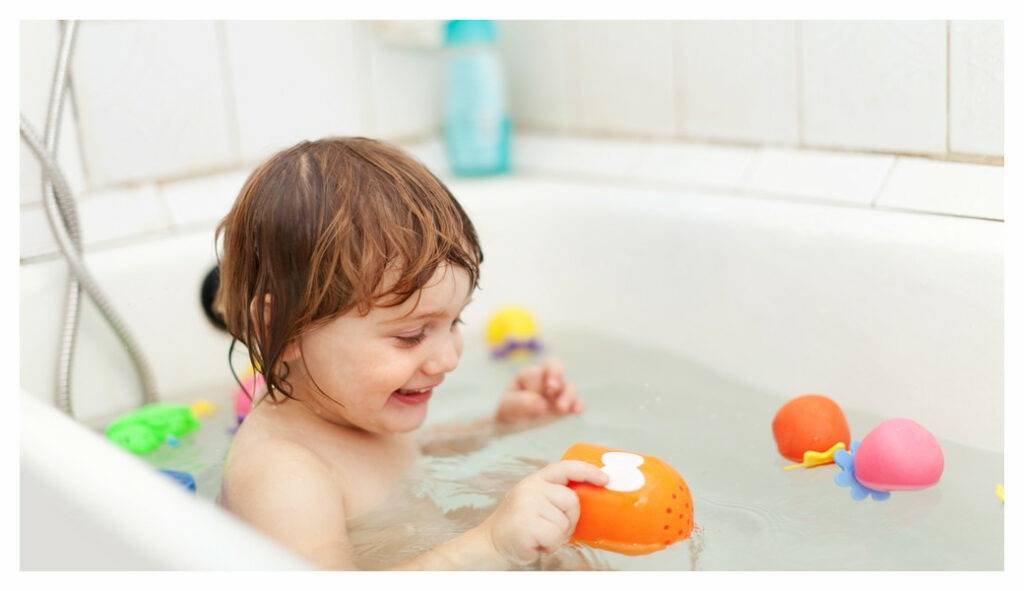 Toddler in bath playing with brightly coloured plastic bath toys. Bath time fun for eczema kids doesn't mean bubbles!