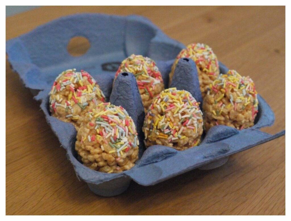 Open egg box containing easter eggs made with rice krispies and marchsmallows covered in colourful sugar strands