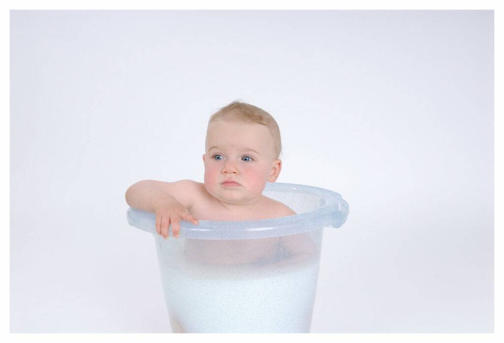 Older baby in bucket style baby bath. The water is a milky white colour from the eczema emollient added to the water