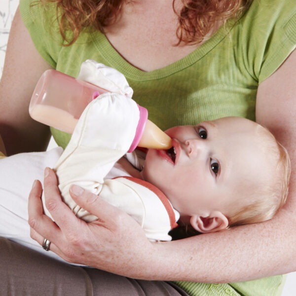 Baby holding a bottle, wearing babies bolero style original cream ScratchSleeves. Shows babies can still use their hands naturally and hold their bottle while their hands are covered by the silk eczema mitts.
