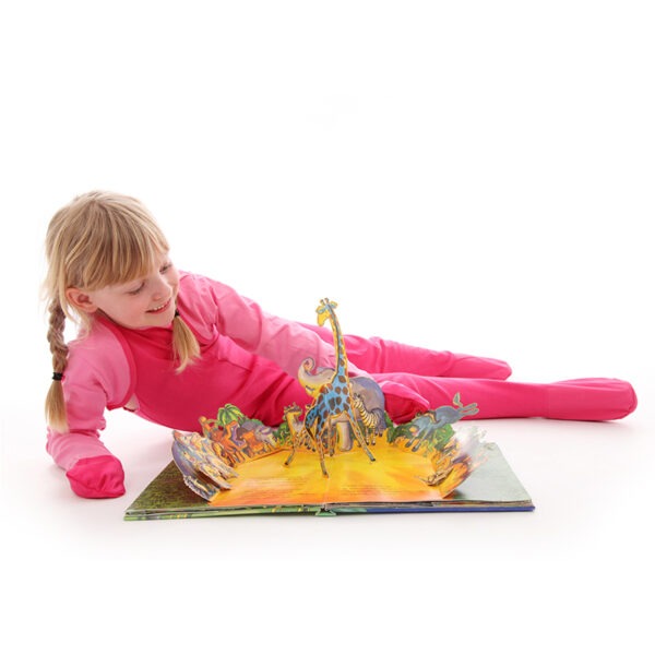 Young girl having fun, wearing happy pink superhero dungarees and ScratchSleeves, while reading a pop up book. Shows children can still play and use their hands naturally while their hands are covered by the silk eczema mitts and eczema skin is protected. Also shows that the products can be layered for extra protection.