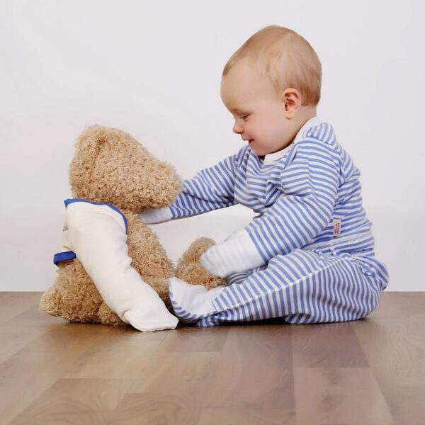 Baby boy sat on floor playing with teddy and wearing ScratchSleeves blue striped babies pyjama set. Shows the pyjama set is a loose, comfortable fit and babies hands can still be used naturally to play. Also shows that eczema clothing does not have to be boring.