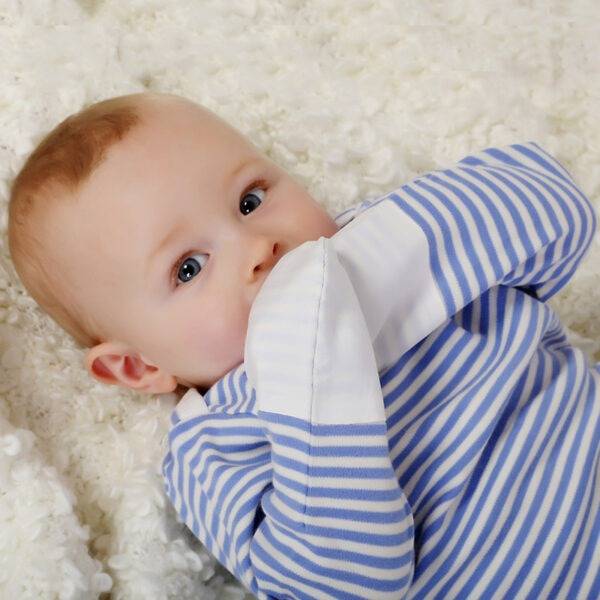 Baby boy with mitts in mouth wearing ScratchSleeves babies striped pyjama top. Shows the pyjama top is safe for babies to chew on the mitts as they are tested for heavy metals. Pyjama top has a blue and white striped body, envelope neckline with a cream trim and white sewn in mitts.