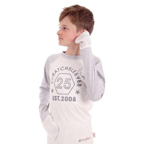 Teen boy wearing ScratchSleeves baseball style pyjama top and rubbing his ear with his left hand. Shows the pyjama tops are comfortable and the mitts are soft. Pyjama top has external shoulder, neck and hem seams. White body with grey printed logo featuring a hexagon and est.2008.