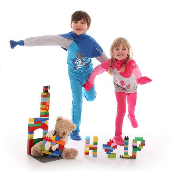 Young boy and girl having fun playing and pretending to be superhero's while wearing ScratchSleeves superhero pyjama sets with capes. Fun eczema pyjama sets in bright colours, with cool bear prints, showing eczema clothing does not have to be boring.