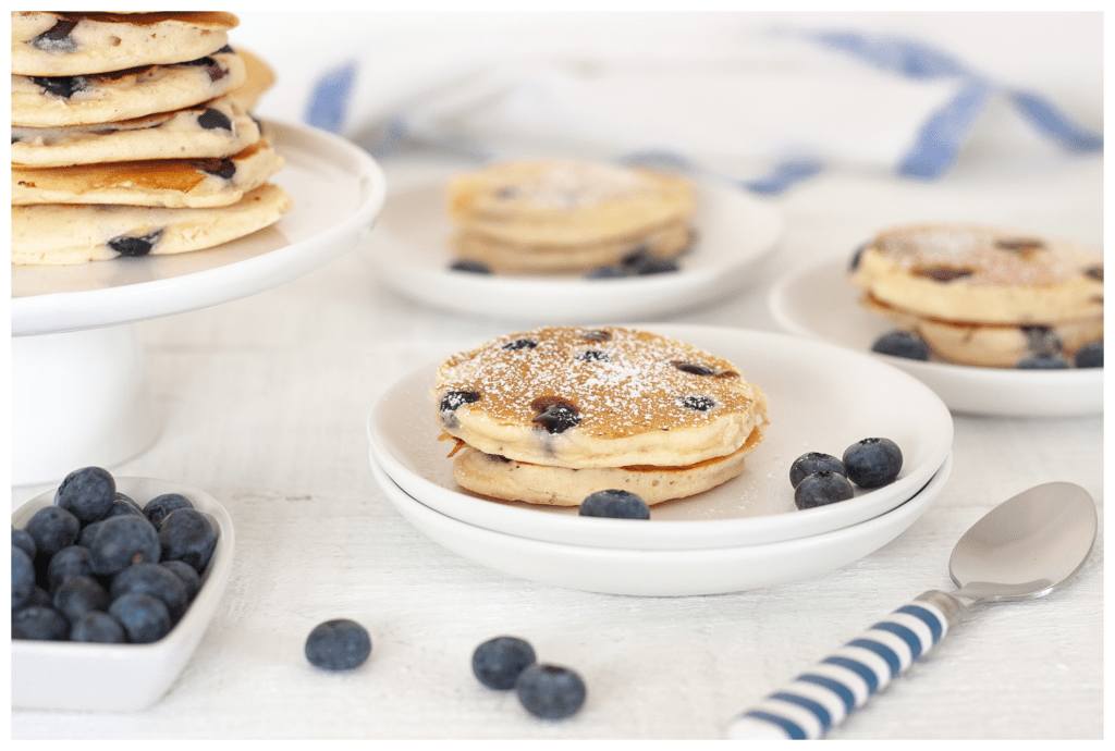 Eczema friendly and tasty blueberry breakfast pancakes stacked on plates with a side of extra blueberries