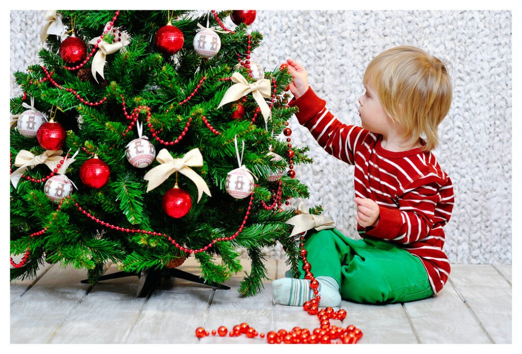 Young child decorating an artificial Christmas tree. The photo is obviously staged as the decorations are far too organised and coordinated for a child to have hung them.