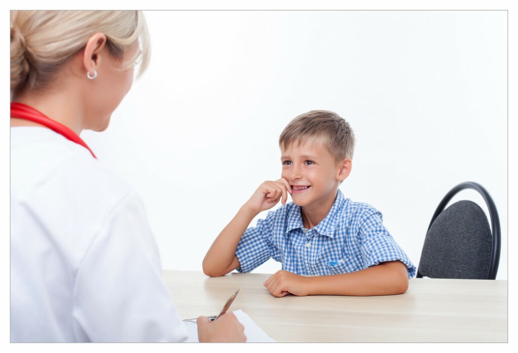 Young boy sitting across a desk from a doctor. He looks a bit in awe. Not ideal for communicating effectively with medical professionals!