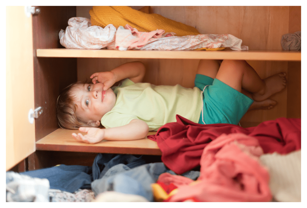 Cheeky child hiding on shelf in their clothes cupboard. The clothes are on the floor in the foreground!