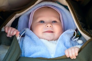 Baby dressed for winter with layered clothing looking out of carry cot