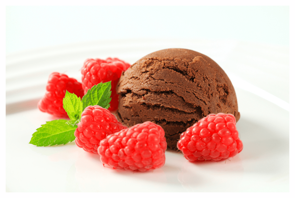 Scoop of dairy free chocolate ice cream on white plate with raspberries on the side.