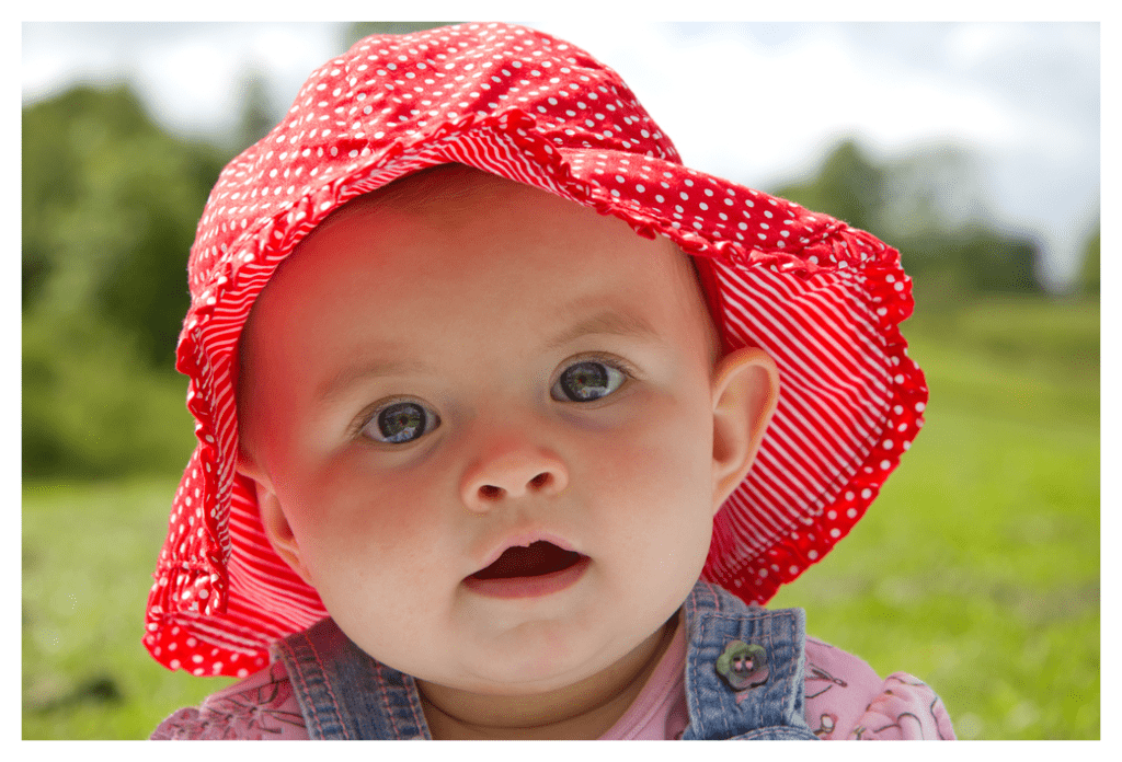 Baby girl wearing red spotted, wide brimmed sunhat on bright sunny day