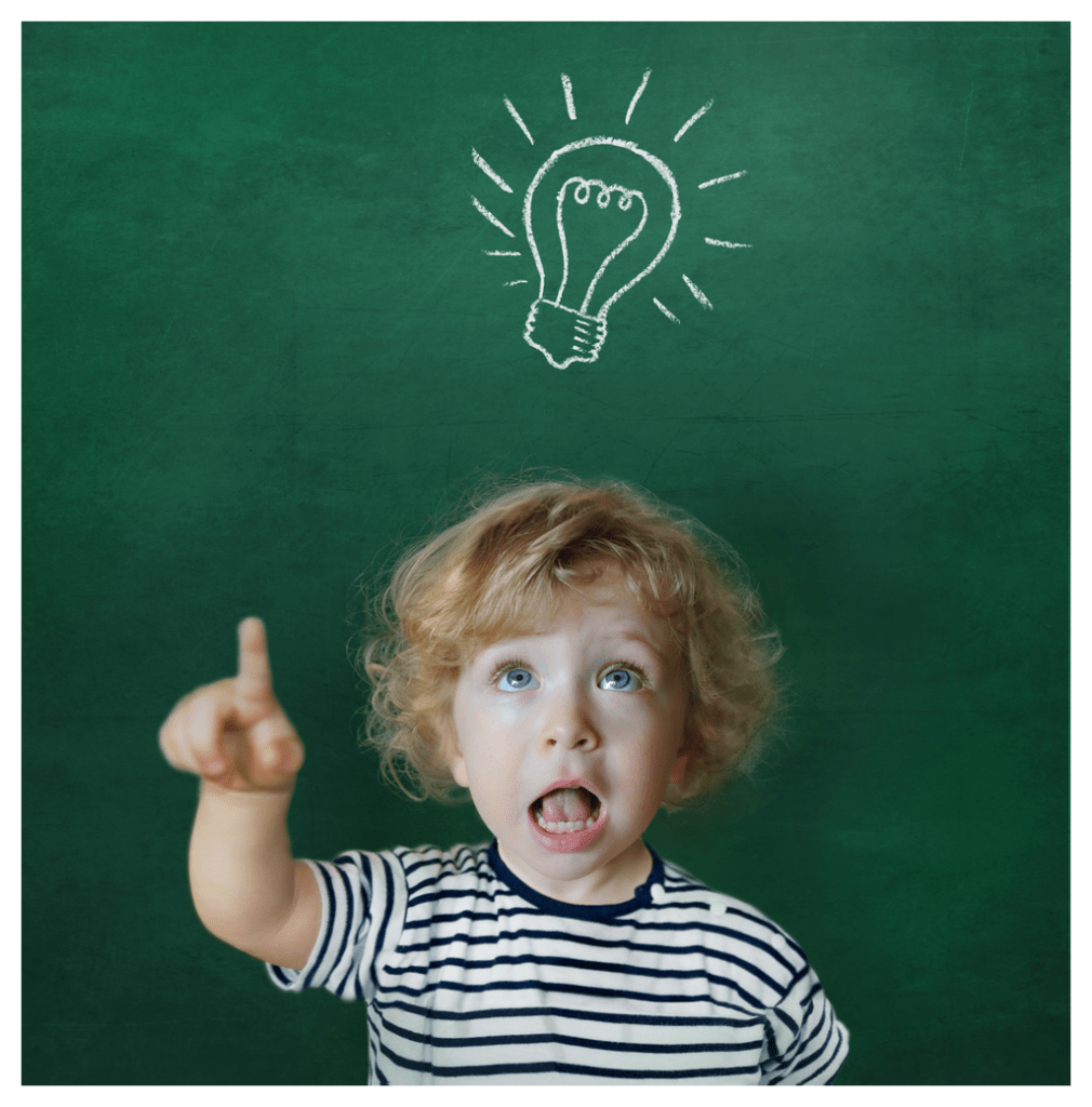 Toddler standing in front of a blackboard with light bulb drawn in chalk above his head. The toddler looks like a bossy teacher.