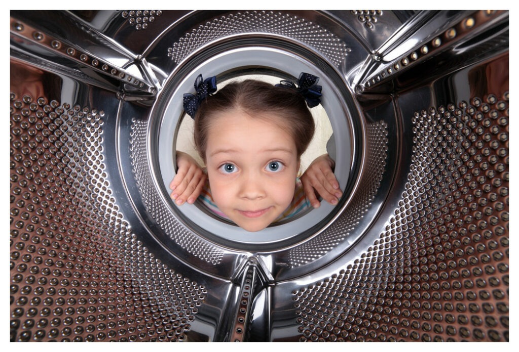 photo taken from inside the drum of a washing machine of young girl with bunches looking into the washing machine.