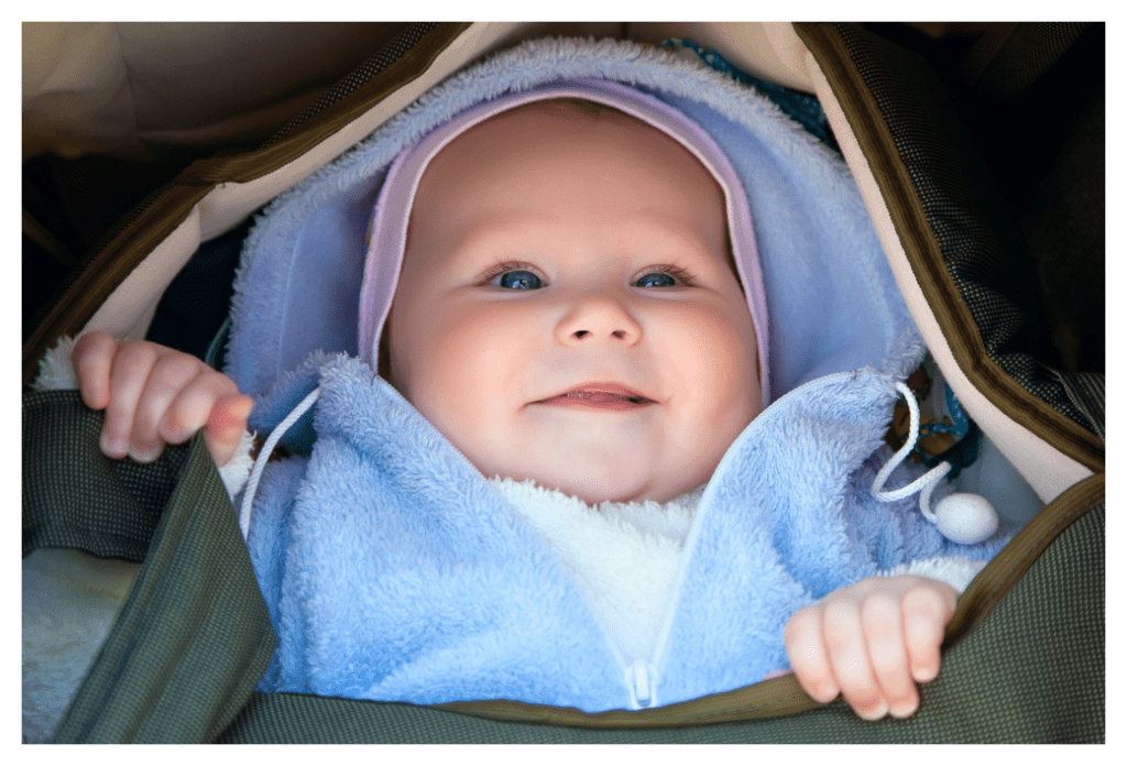 Baby dress in multiple layers of thin fleece looking out of a carry cot. He looks snug and warm but ready to get out and see the world
