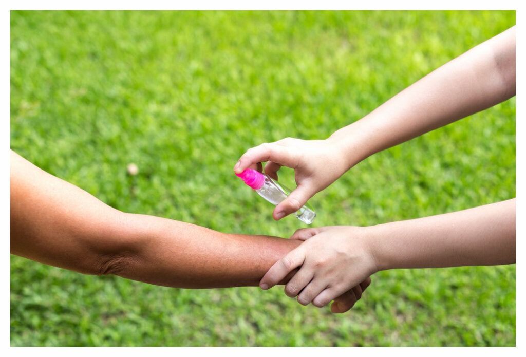 Adult spraying insect repellent on child's bare arm