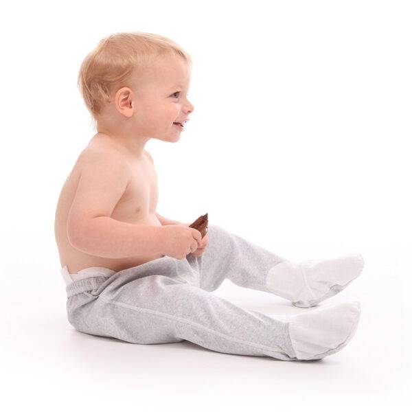 Little boy sat eating and wearing ScratchSleeves toddlers grey marl pyjama bottoms with sewn in feet. Shows that the pyjama bottoms are a comfortable fit and have no inside leg seams. The pyjama bottoms have closed feet with a layer of white, 100% woven cotton over the front of the foot, under the toe and inside the ankle.