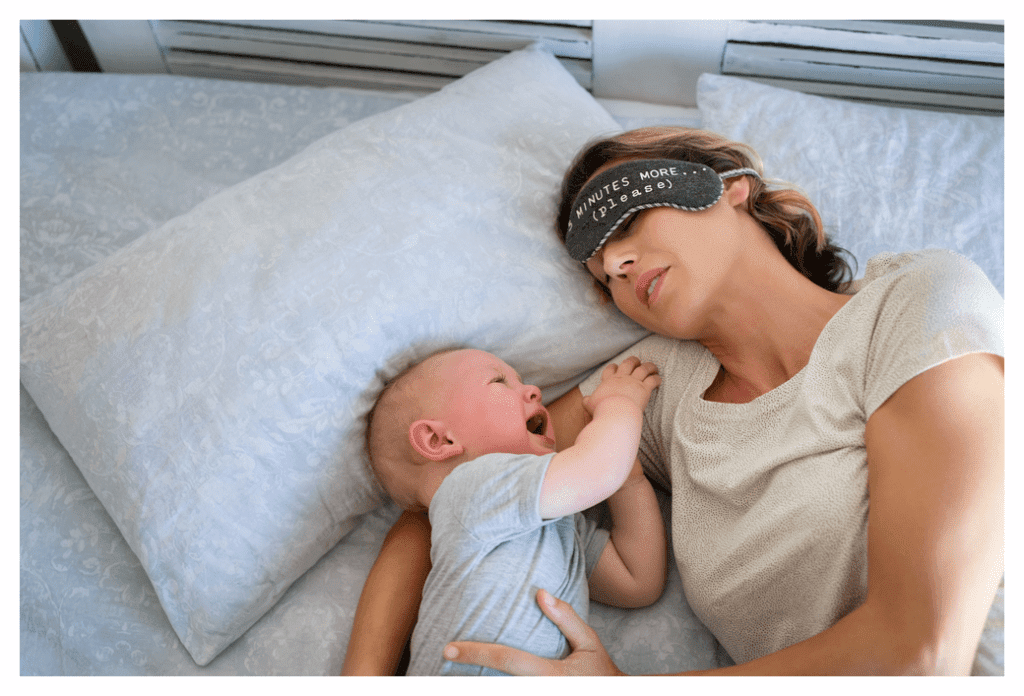 Exhausted mum lying on double bed wearing eye mask (which reads 5 minutes more (please) cuddles crying baby 