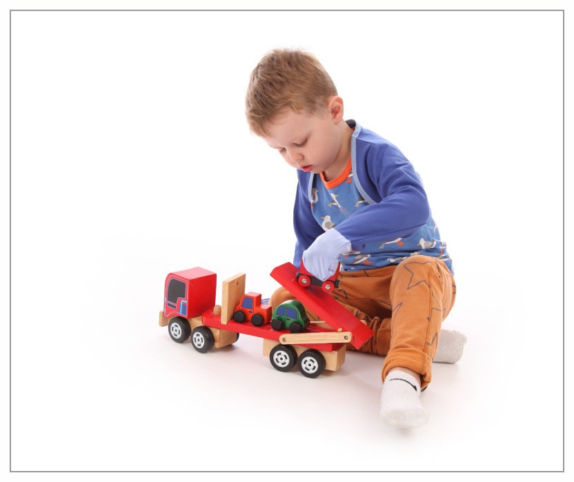 Toddler boy wearing scratch mitts and playing with chunky wooden cars and car transporter lorry. The scratch mitts has obviously not getting in the way of his play.