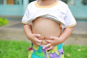 Young boy with white and yellow t-shirt pulled up exposing his tummy. His hands are holding his tummy