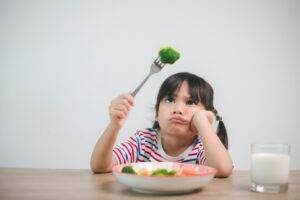 Little girl looking very unimpressed holding fork with a piece of brocoli