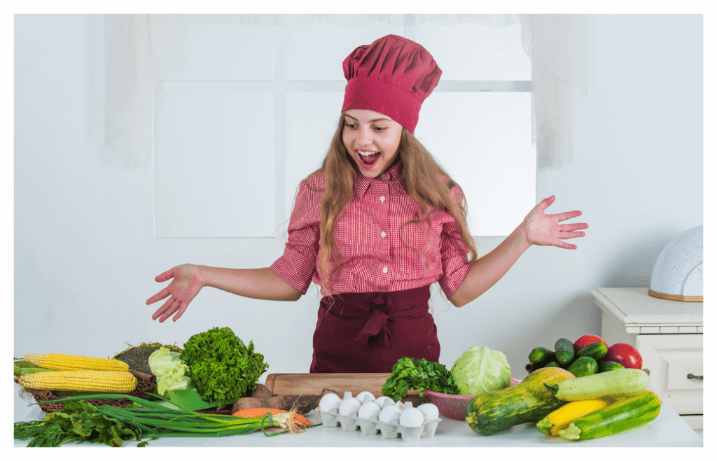 Teenage girl in chef's hat and apron hamming it up looking worktop covered with colourful healthy food rich in eczema friendly vitamins and minerals