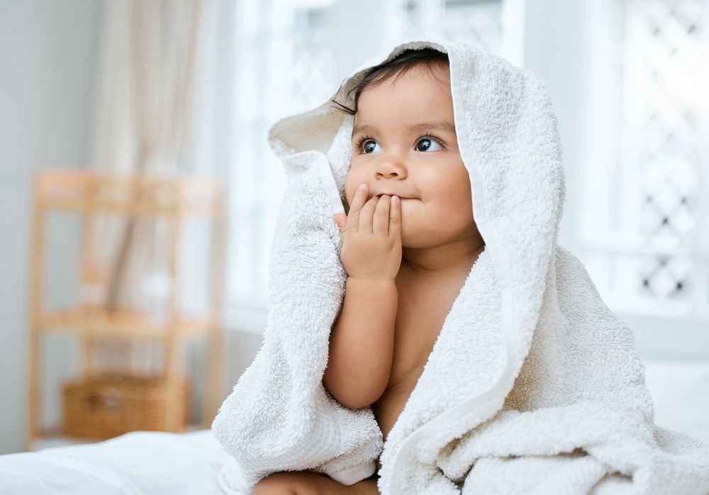 Toddler with big brown eyes wrapped in white towel following bath