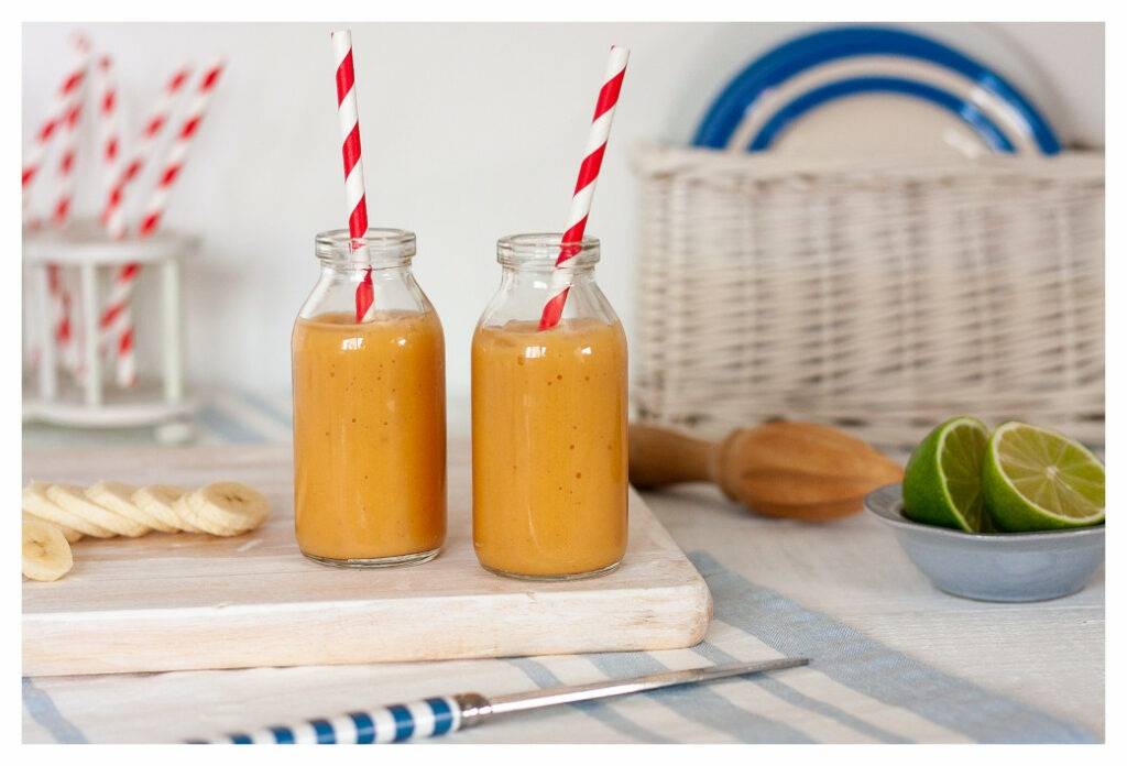 Eczema friendly papaya and banana smoothies, served in mini milk bottles with red and white striped paper straws. The orange smoothie contrasts with the blue and white background.