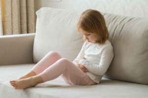 Young girl sitting on sofa holding her stomach and looking sorry for herself.